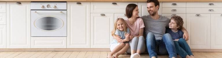 happy family sitting on wood plank flooring in kitchen hero | America's Carpet Barn